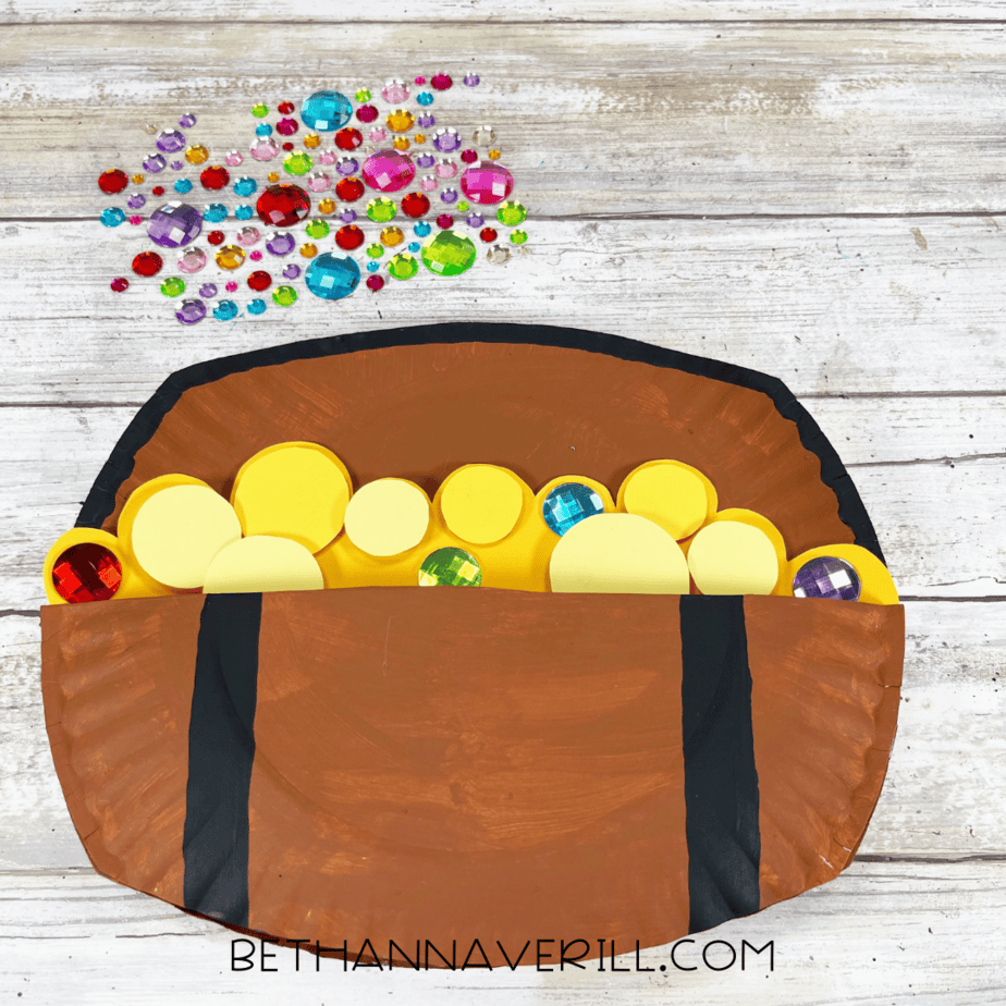Paper plate treasure chest filled with yellow paper coins and colorful craft gems.