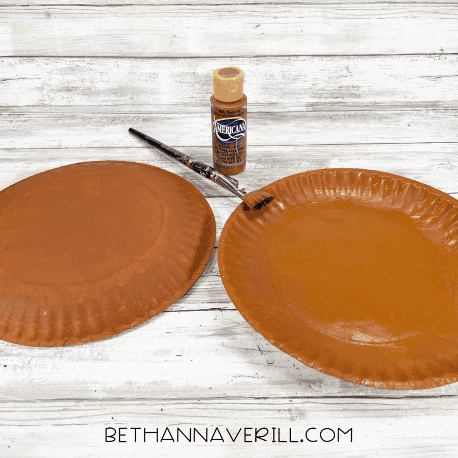 Two paper plates painted brown with paintbrush and bottle of brown paint.