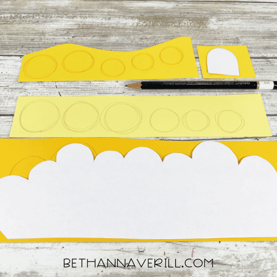 Yellow construction paper with drawn circles and chest details sketched in pencil.