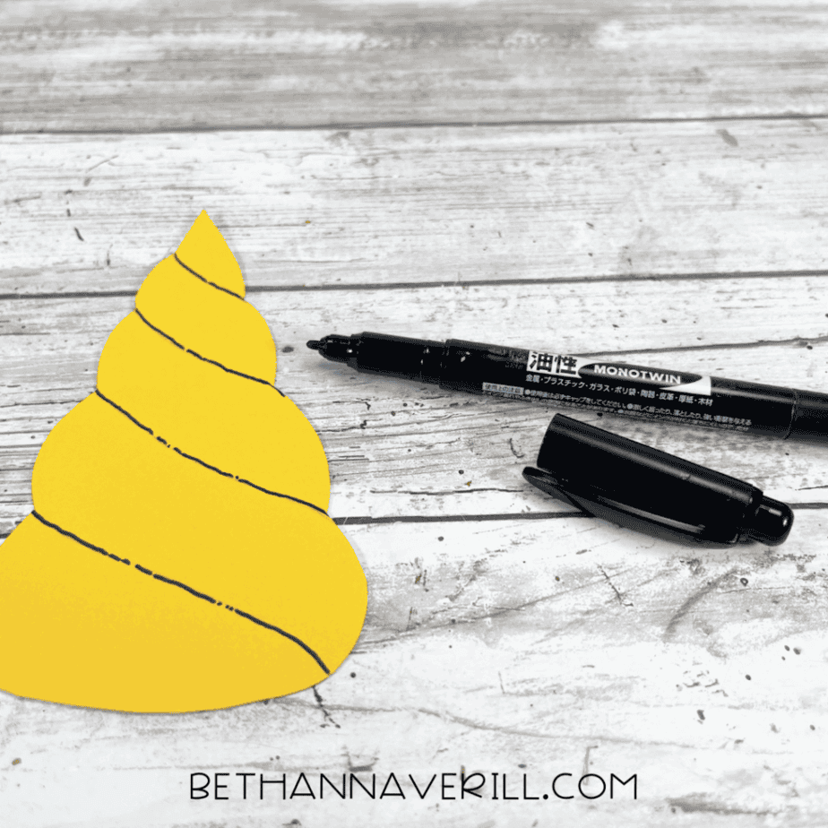 Yellow unicorn horn with black marker details drawn on it.