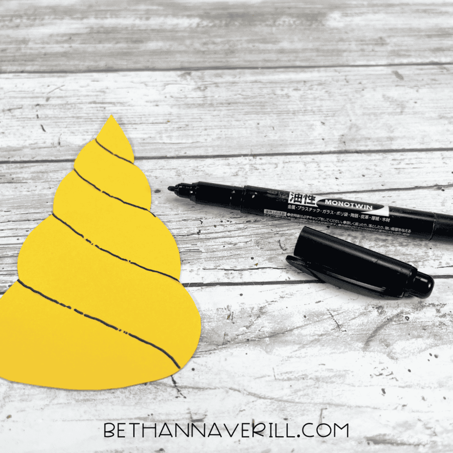 Yellow unicorn horn with black marker details drawn on it.