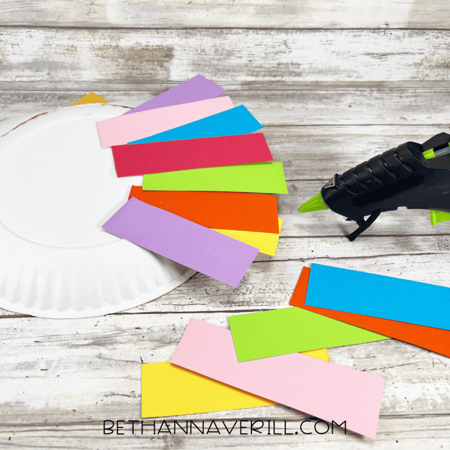 Paper plate with rainbow mane strips being glued to the back.