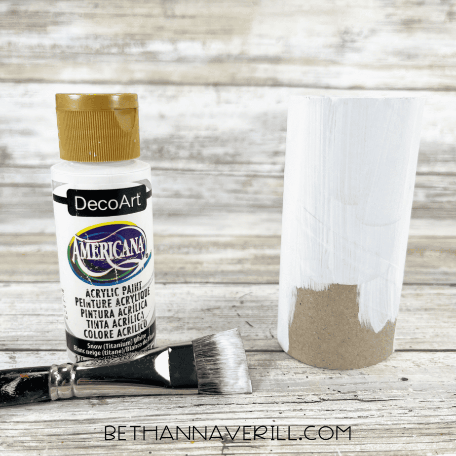 Toilet paper roll partially painted white with white acrylic paint and paintbrush.