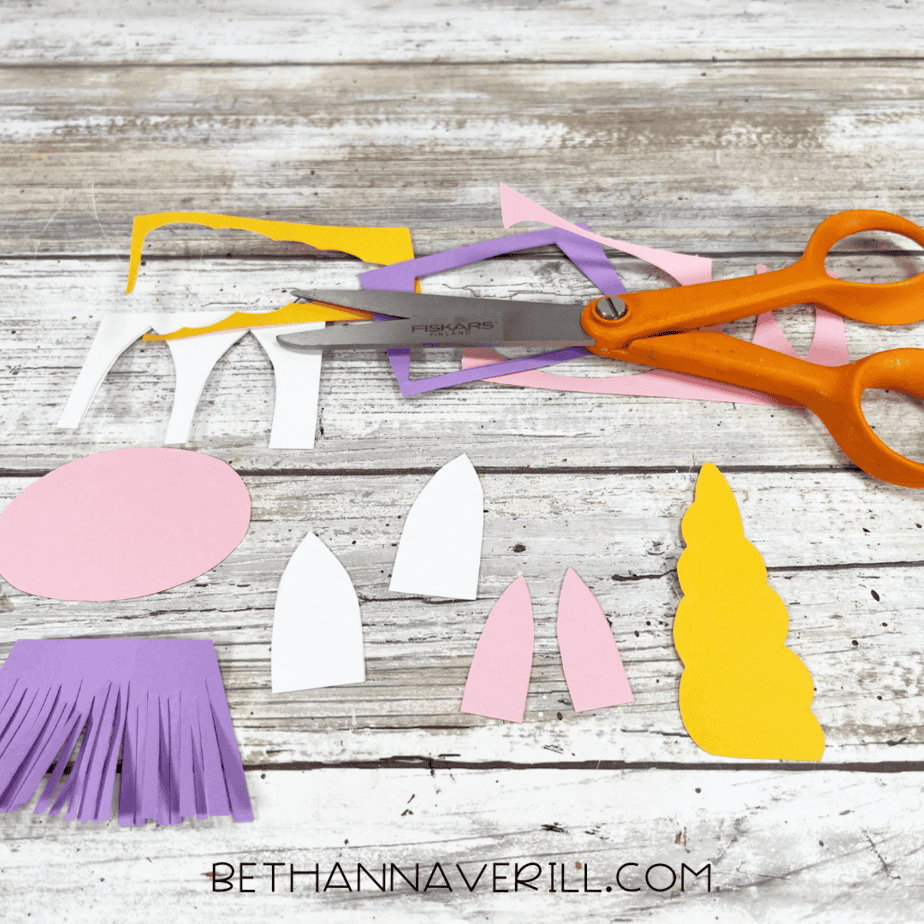 Unicorn craft paper pieces cut out and ready to assemble, with scissors beside them.