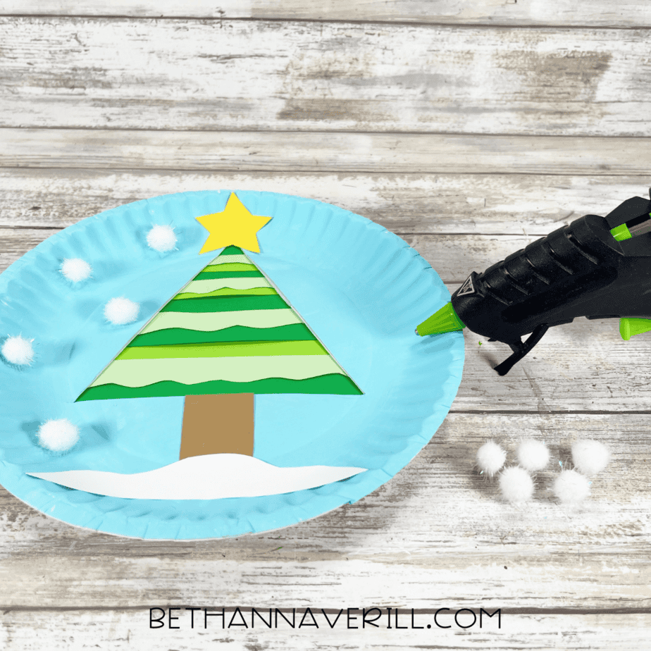 Paper plate with cotton balls and white paper snowbank added around the tree.
