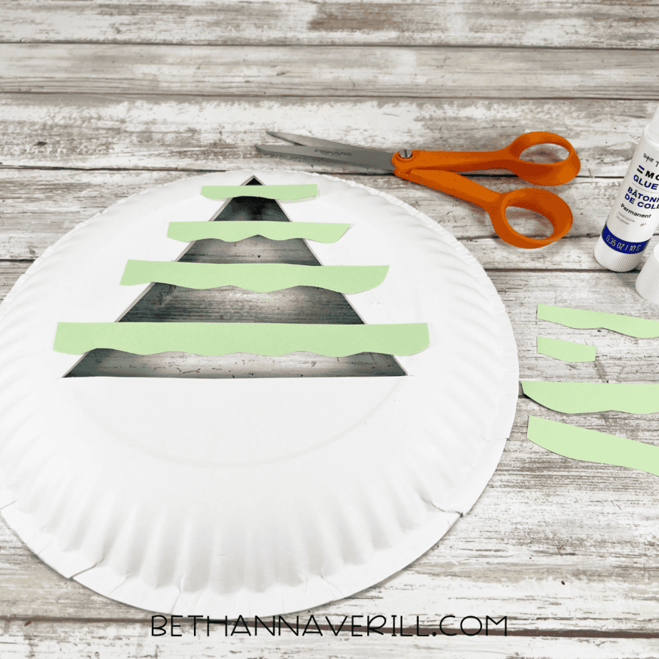 Paper plate flipped over with wavy green paper strips glued behind triangle cutout.