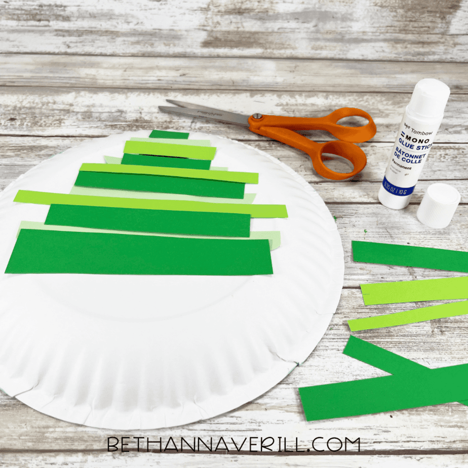 Paper plate showing multiple green strips layered behind triangle shape for tree.