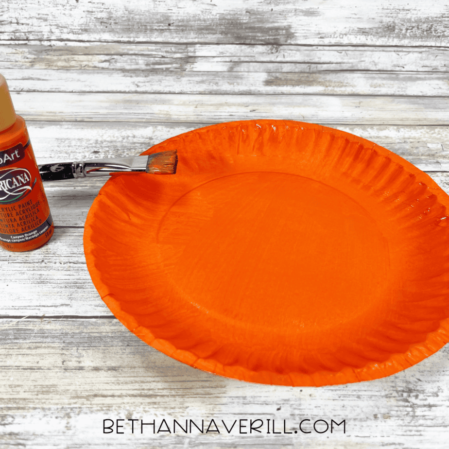 Paper plate painted bright orange with paintbrush beside it.