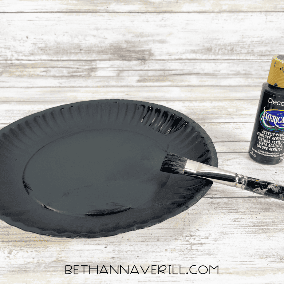 Paper plate painted black with paintbrush beside it.