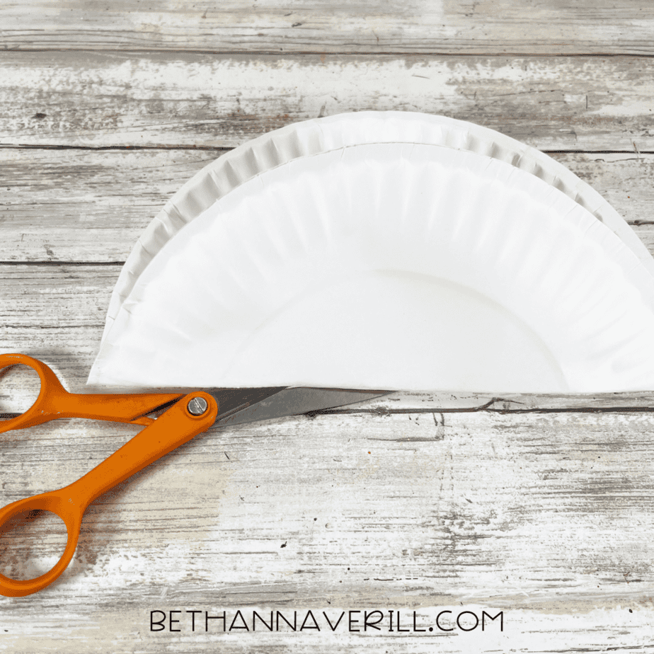 Paper plate folded in half with scissors ready to cut.