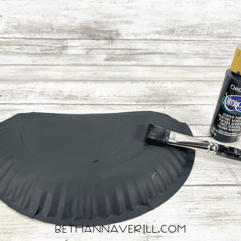 Paper plate painted black with paintbrush beside it.