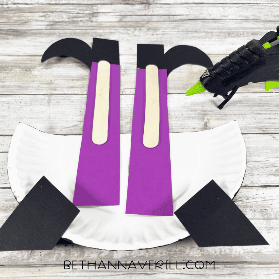 Witch legs glued to back of paper plate cauldron with glue gun visible.