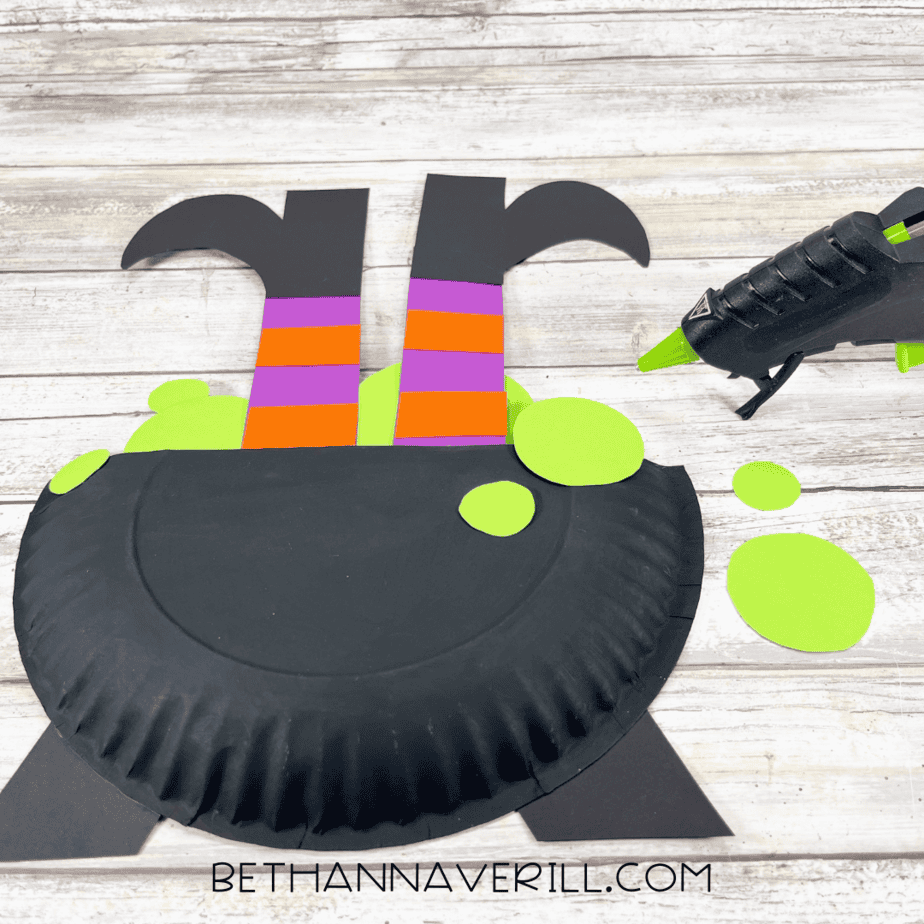 Black paper cauldron with witch legs and green bubbles being glued in place.