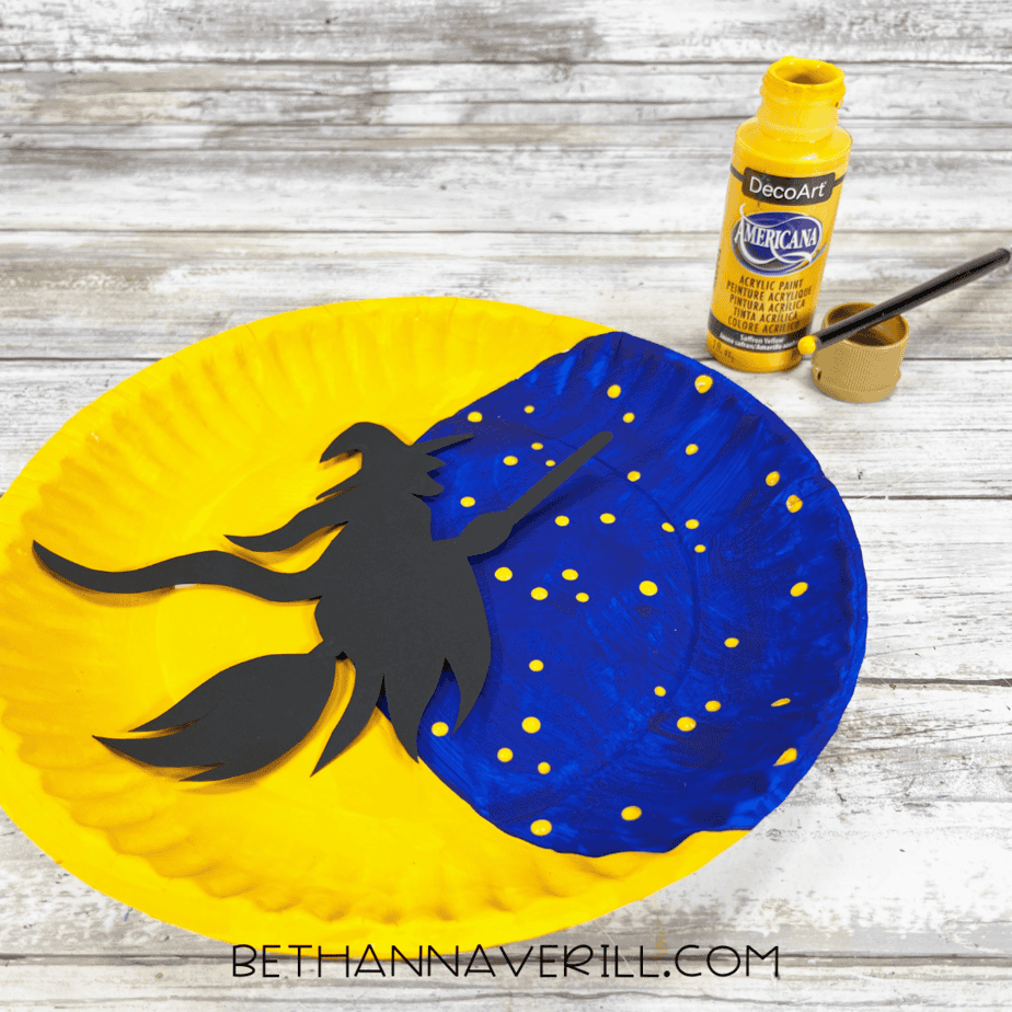 Adding yellow paint dots to blue night sky with paintbrush handle for stars.