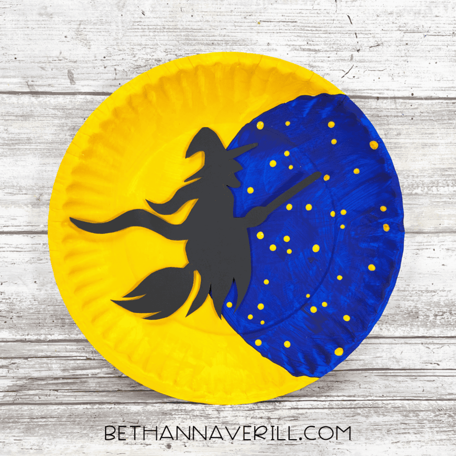 Finished witch moon paper plate craft with black witch flying across starry sky.