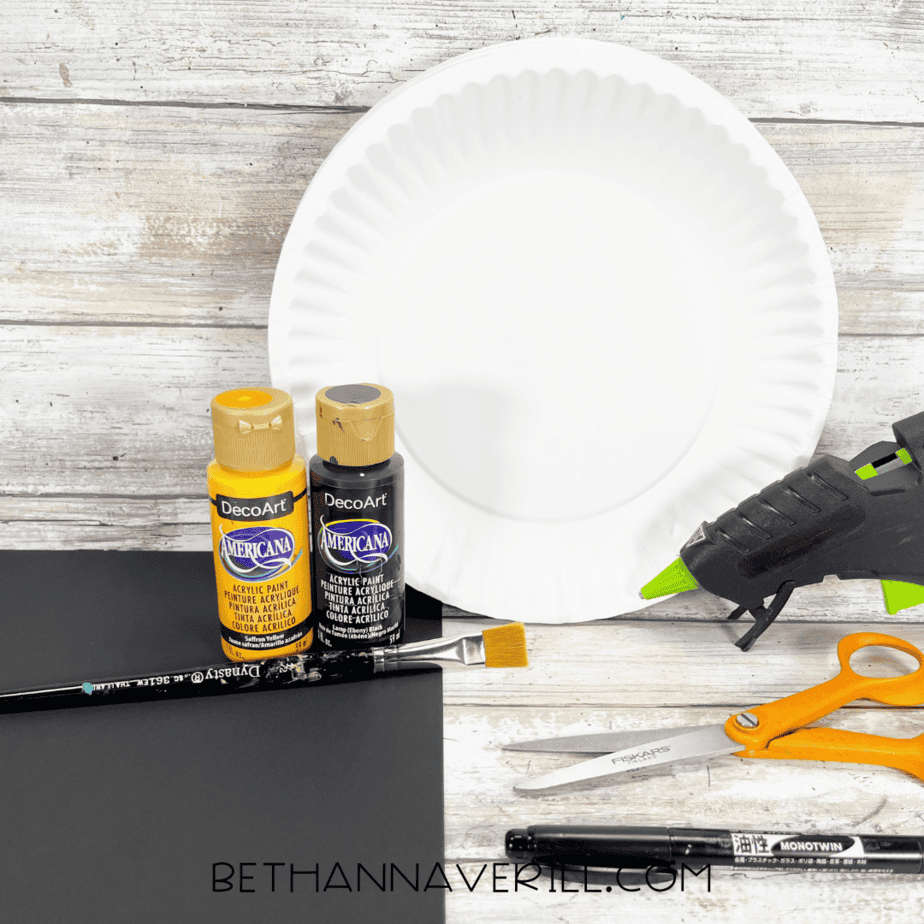 Materials for witch moon paper plate craft including paint, paper plate, glue gun, and scissors.