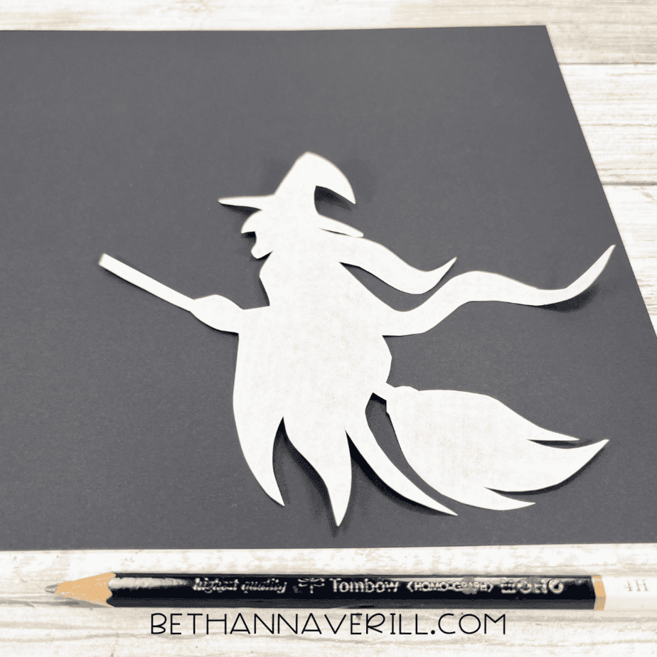 Witch silhouette template placed on black construction paper with pencil for tracing.