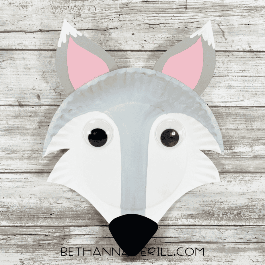 The completed Arctic fox paper plate craft featuring a gray and white face, large googly eyes, black nose, and pink-and-gray ears.