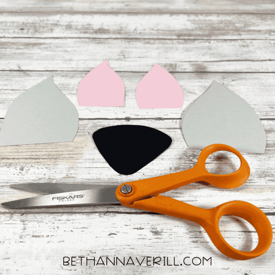 Cutout cardstock pieces for the Arctic fox ears and nose placed next to orange scissors on a wooden background.