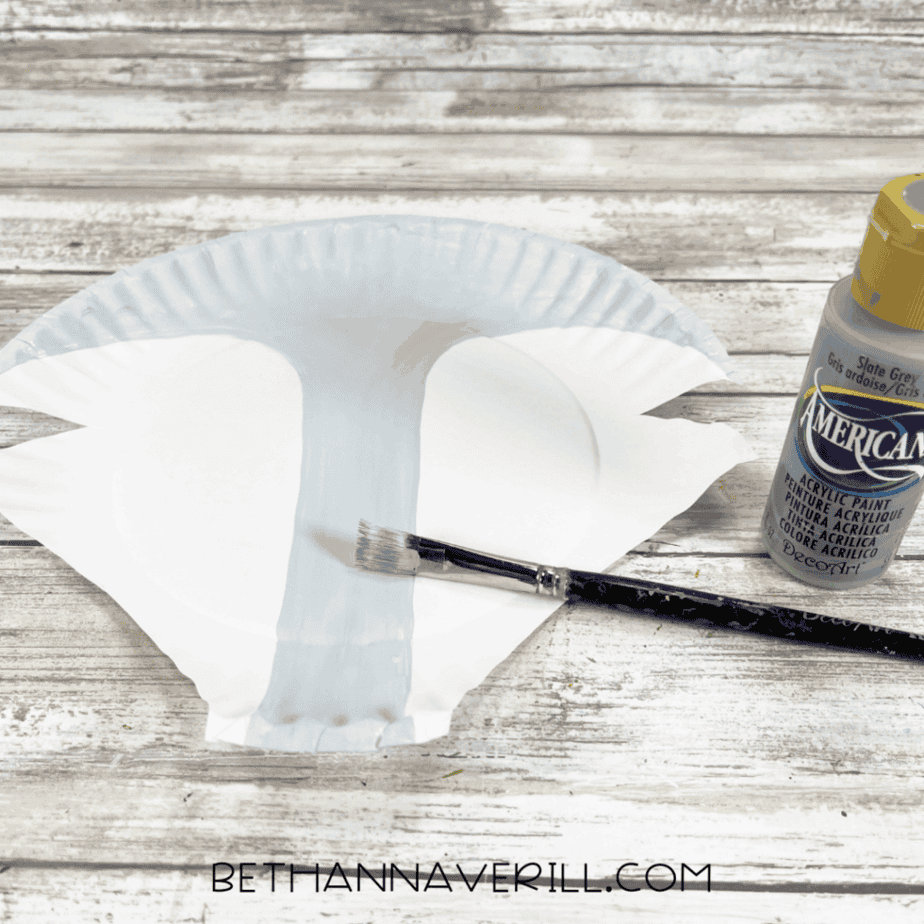 The paper-plate Arctic fox head with the center painted light gray, a paintbrush resting nearby, and a bottle of gray craft paint.
