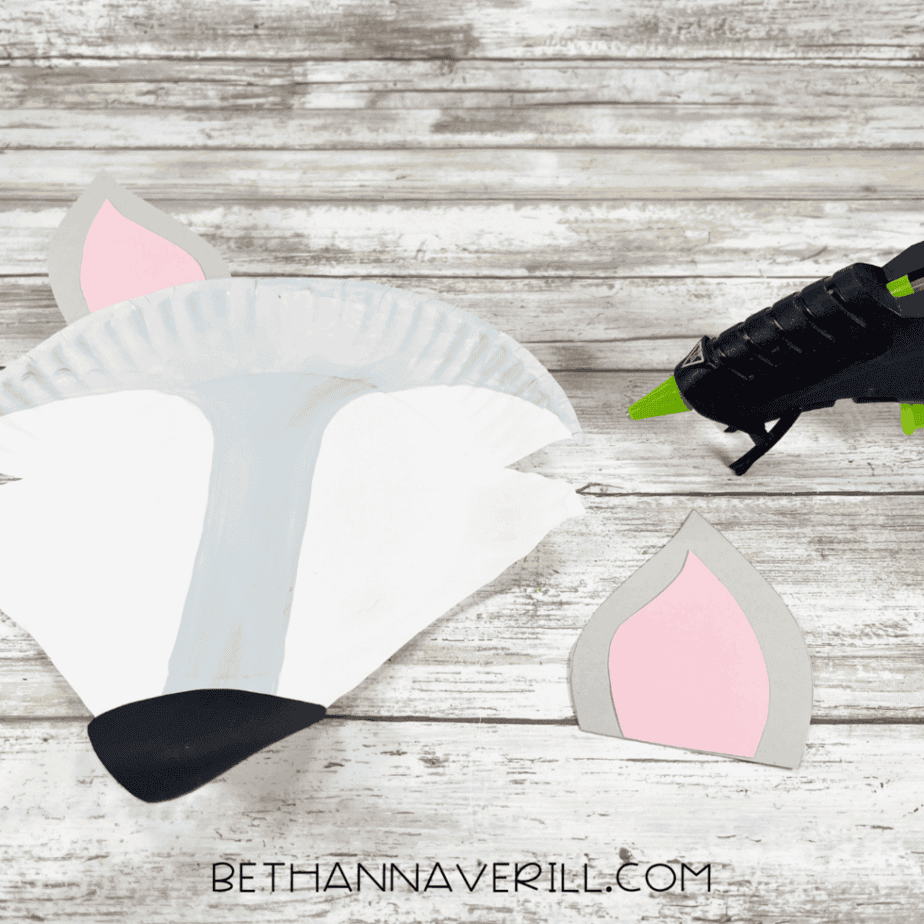 The paper-plate Arctic fox head with pink and gray cardstock ears glued in place and a black cardstock nose added at the bottom.