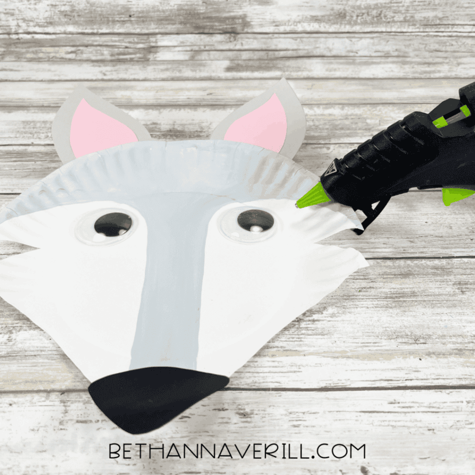 Googly eyes being glued to the Arctic fox face using a hot glue gun.