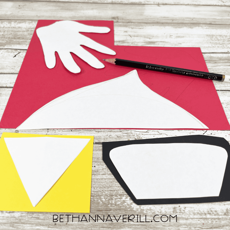 Cardinal craft templates traced onto red, yellow, and black cardstock with a pencil, including a wing, face shape, beak, and handprint wings.
