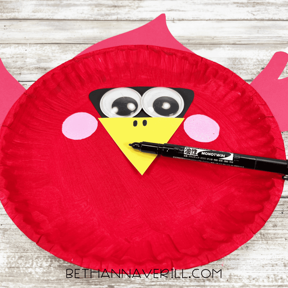 A close-up of the cardinal craft face with the black marker adding two small dots for nostrils on the yellow beak.