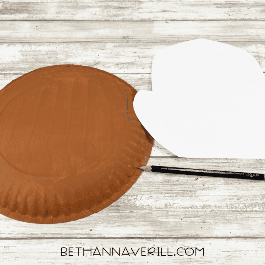 Brown painted paper plate with a moose head pattern laid beside it while tracing the outline with a pencil.