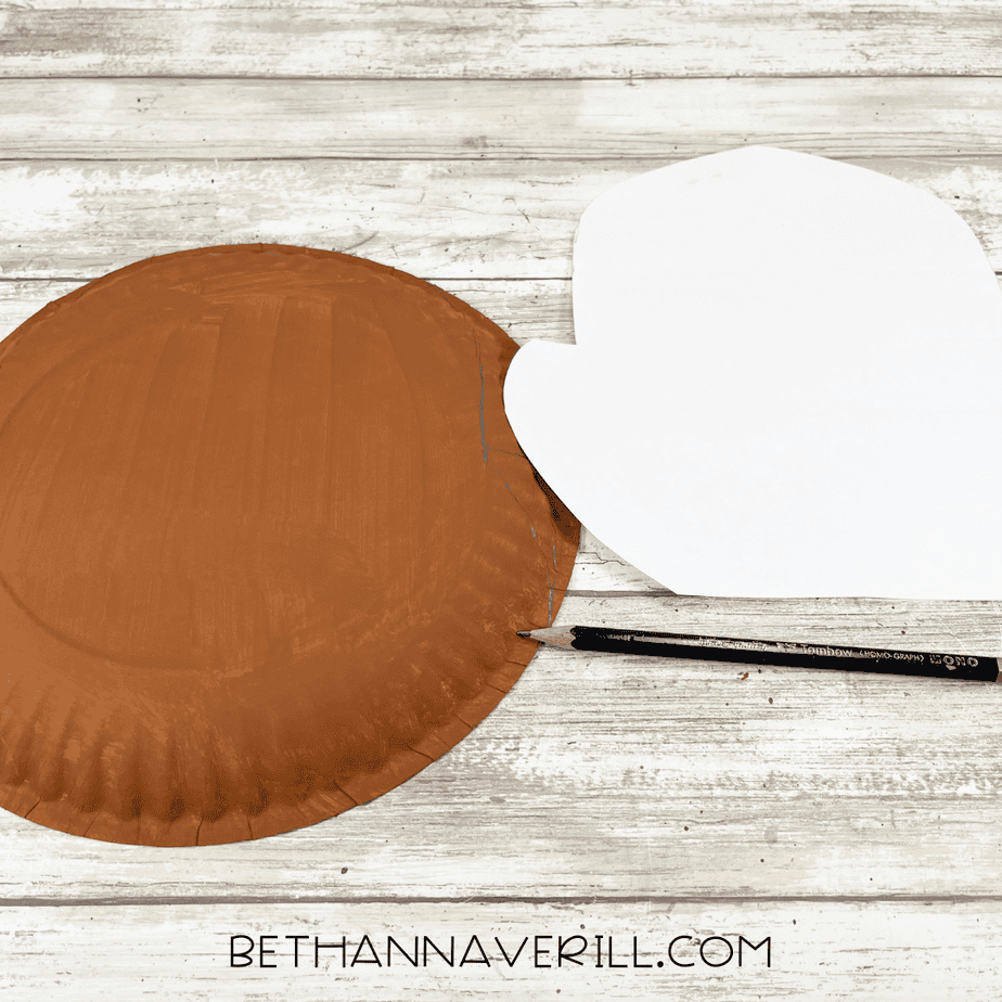 Brown painted paper plate with a moose head pattern laid beside it while tracing the outline with a pencil.