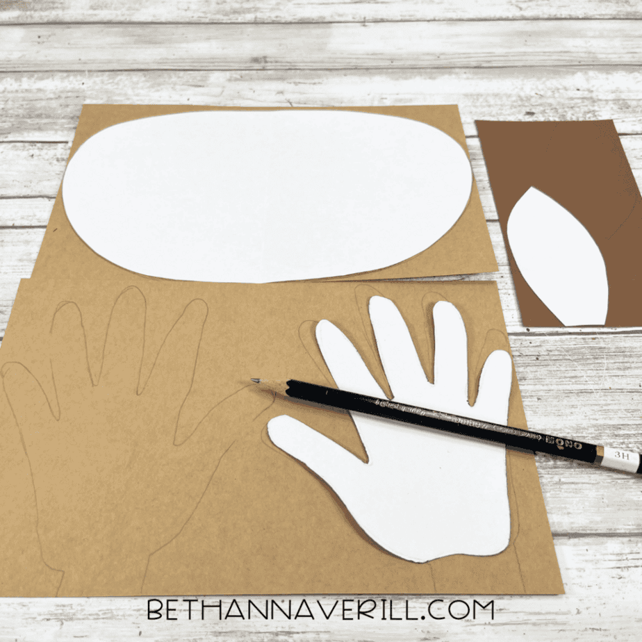 White moose face template, handprint antlers, and ear shapes traced onto brown cardstock with a pencil.