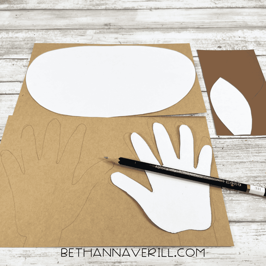 White moose face template, handprint antlers, and ear shapes traced onto brown cardstock with a pencil.