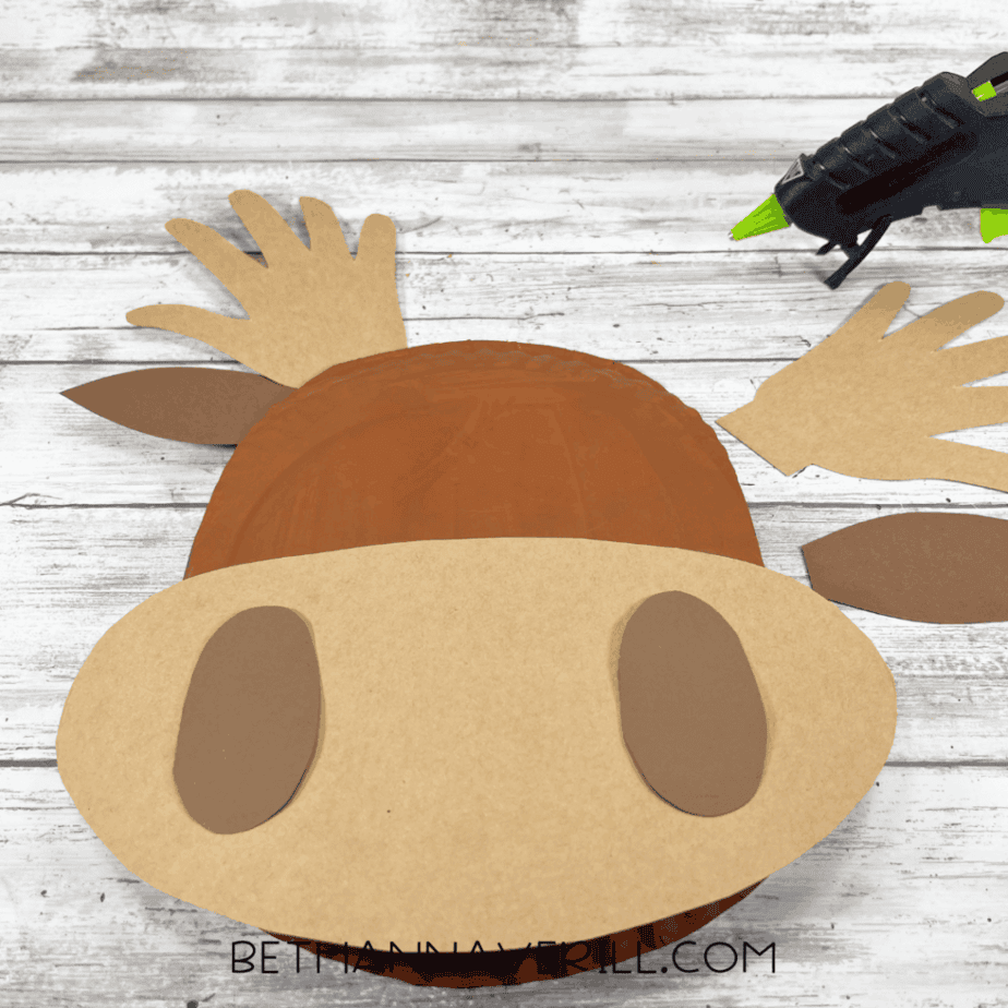 Paper plate moose head with muzzle and ear pieces glued on, and the glue gun visible nearby.