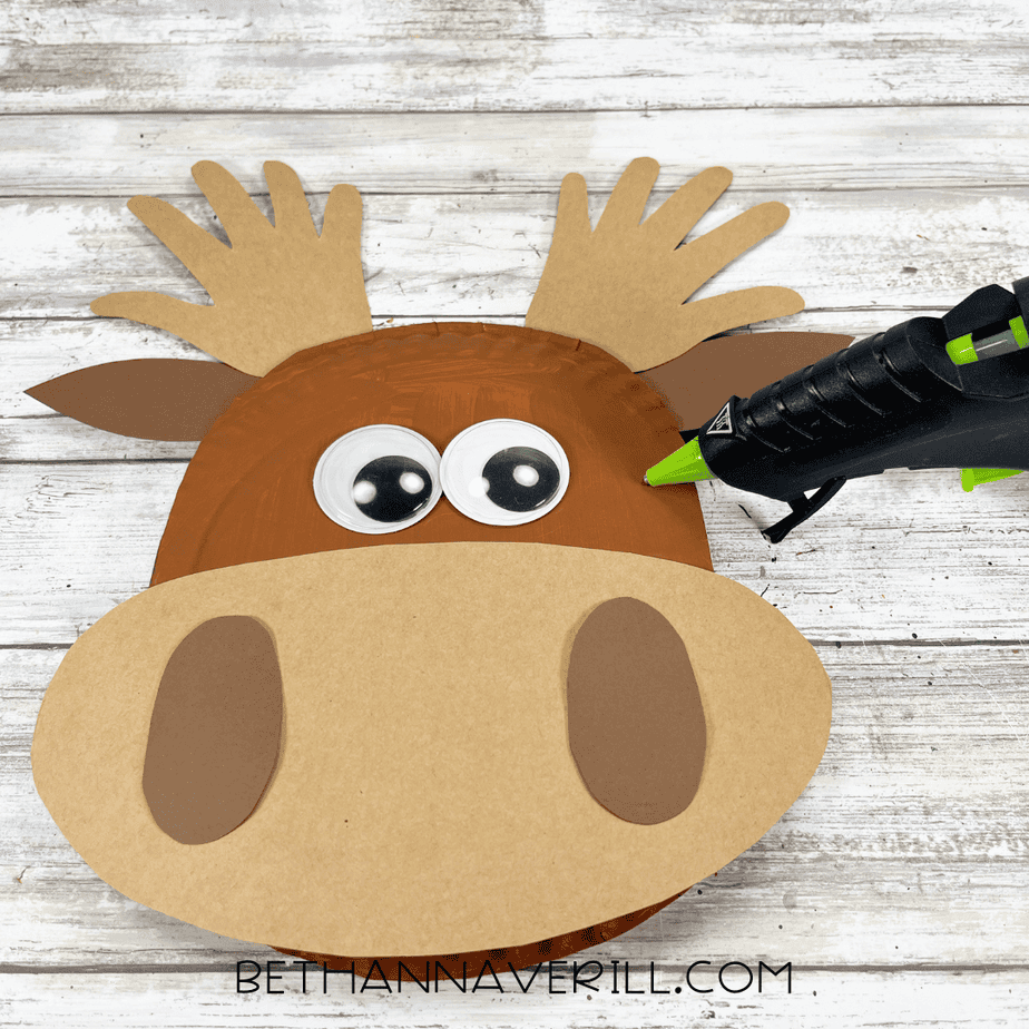 Googly eyes added to the moose craft while a glue gun sits beside it.