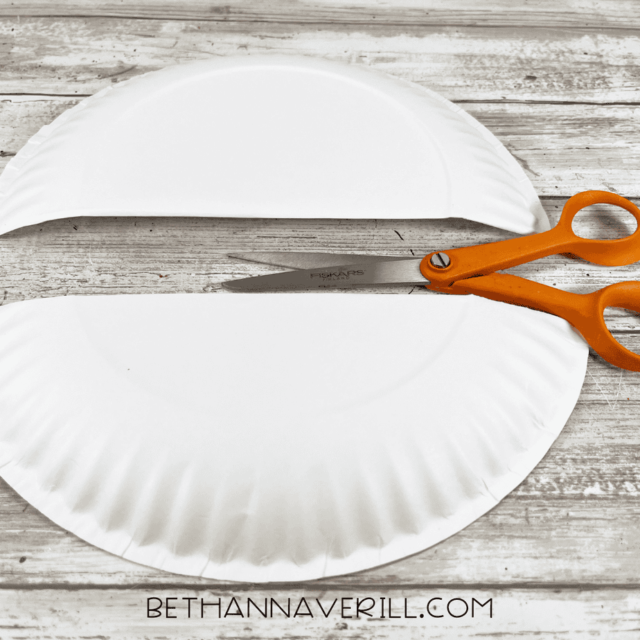 Paper plate cut in half horizontally with scissors placed beside it for the first step of the orca craft.