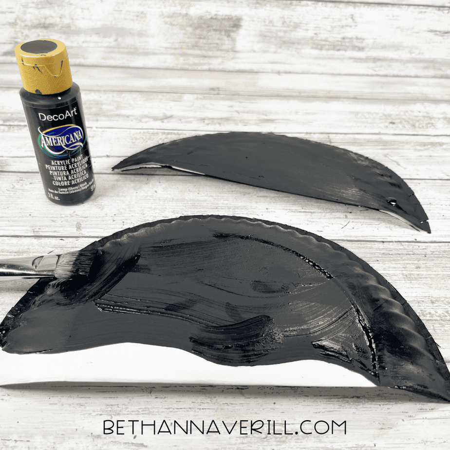 Two paper plate halves being painted black to create the top of the orca for the craft.