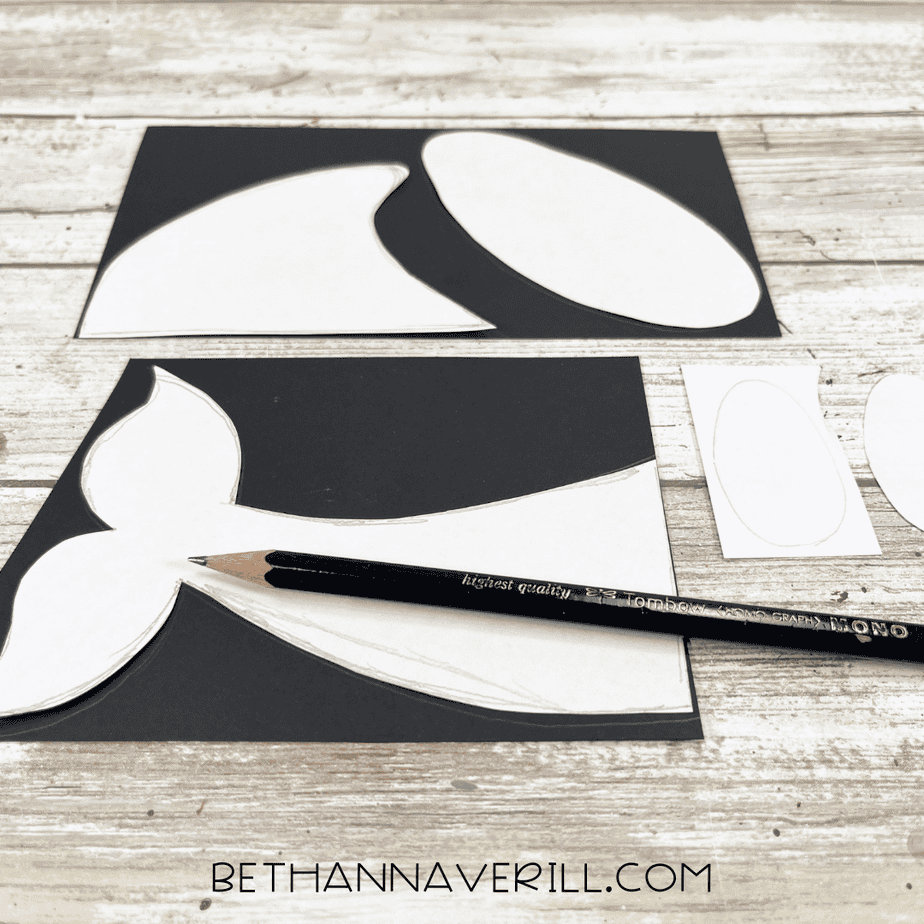 Orca pattern pieces traced onto black and white cardstock using a pencil, ready to be cut out.