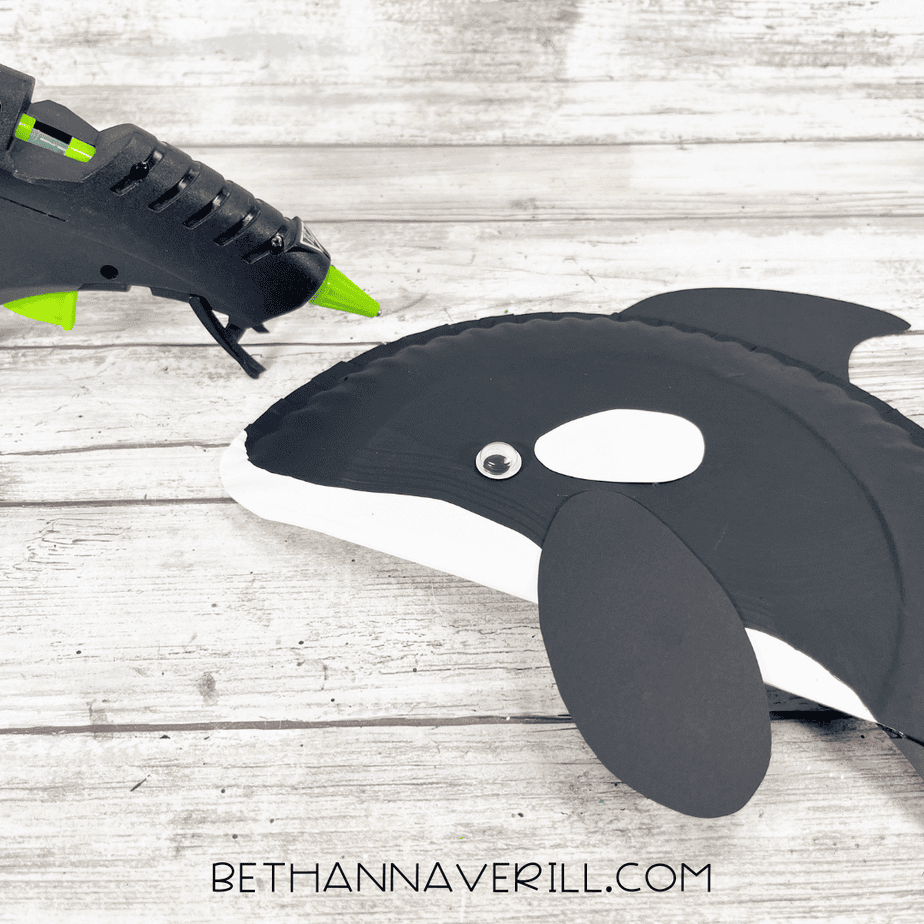 Googly eye and white patch being glued onto the orca’s head section during assembly.