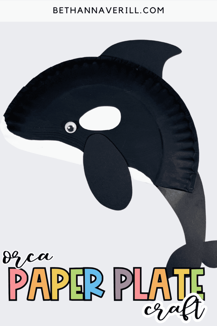 Black-and-white orca paper plate craft made from a cut paper plate with a painted black top, white underside, black flippers, a curved tail, and a googly eye. Displayed on a light gray background with the text ‘Orca Paper Plate Craft.