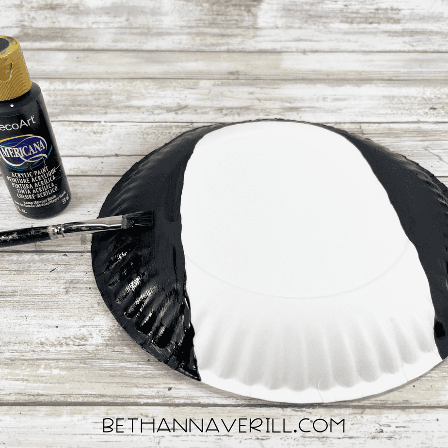 Paper plate upside down with the sides being painted black, showing a white oval belly left unpainted in the center.