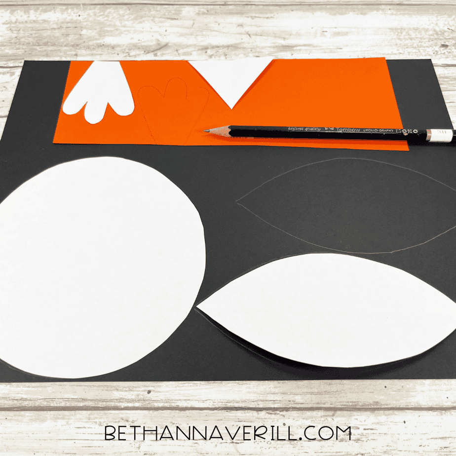 Penguin pattern pieces traced onto black and orange cardstock using a pencil, with white pattern templates nearby.