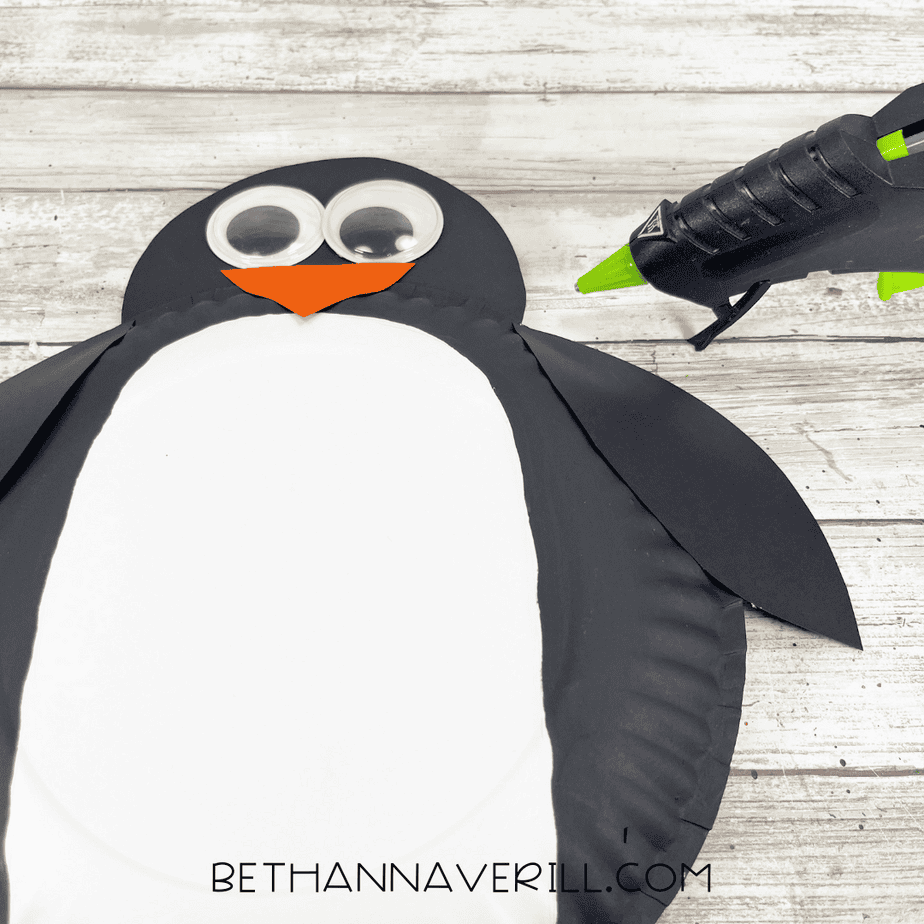 Googly eyes and an orange beak glued onto the penguin’s head with a glue gun positioned beside it.