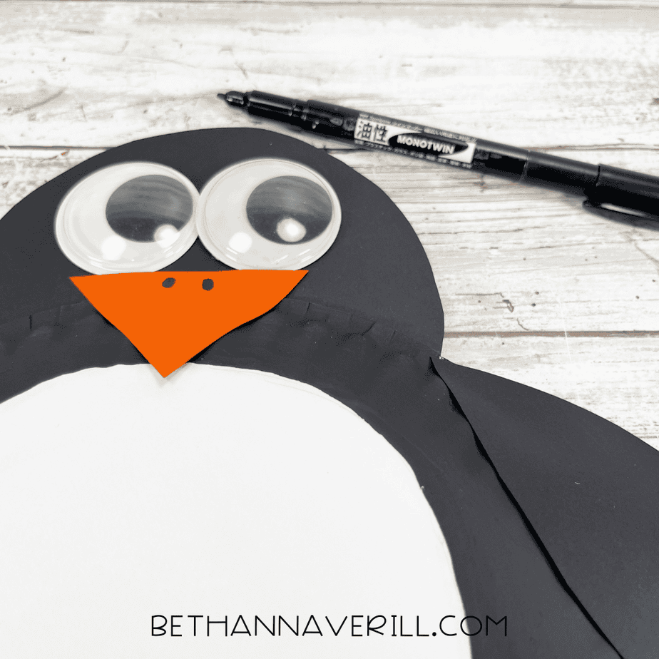 Close-up of the penguin face while a black marker adds nostril details to the orange beak.