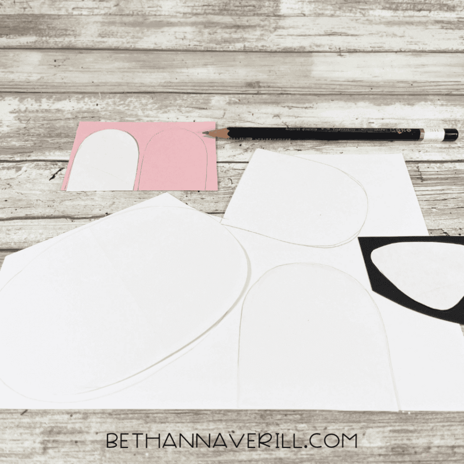 Paper templates for the polar bear’s face, ears, and muzzle traced onto white and pink cardstock with a pencil, arranged neatly on a wooden table.