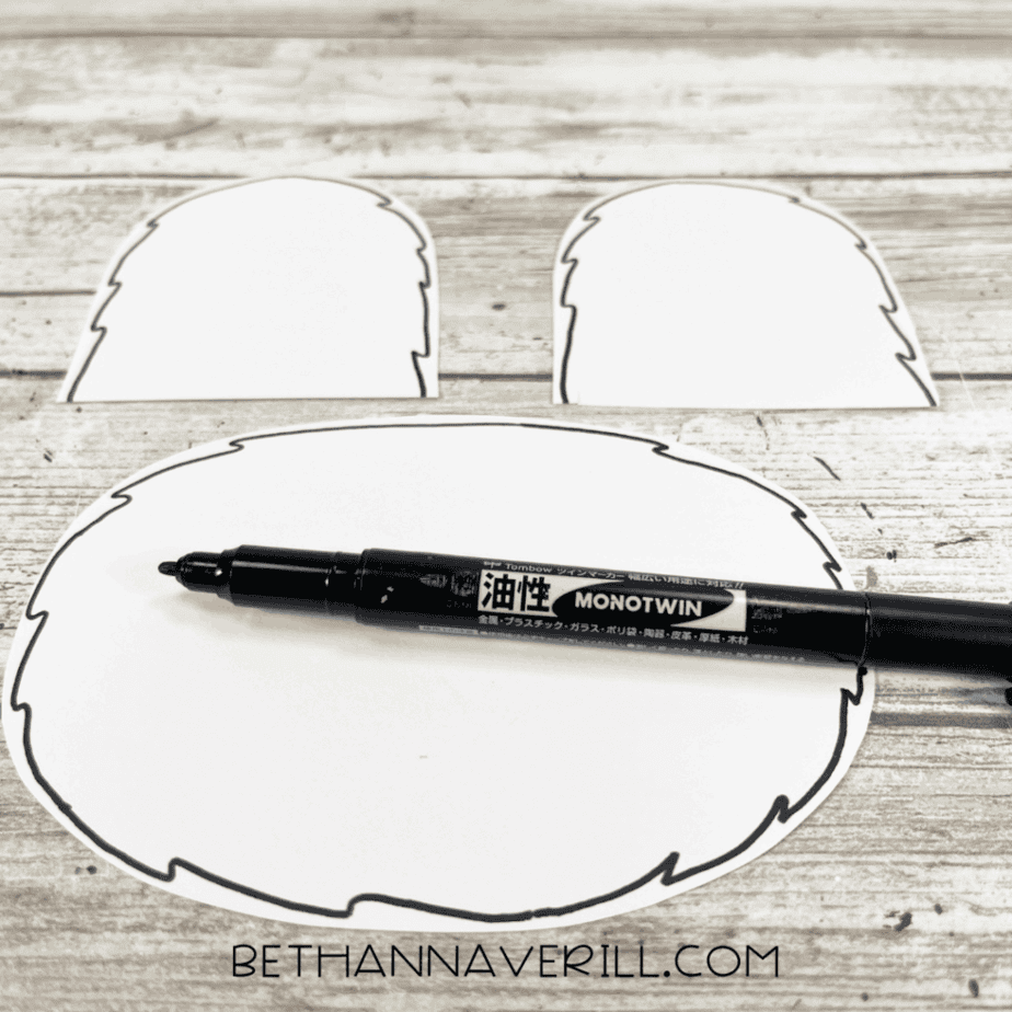 A black permanent marker adding simple fur outline details to the polar bear’s muzzle and ears on white cardstock.