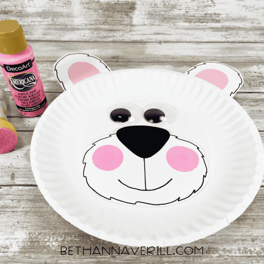 Pink sponge-painted cheeks being added to the polar bear’s muzzle while pink acrylic paint and a small sponge sit next to the craft.