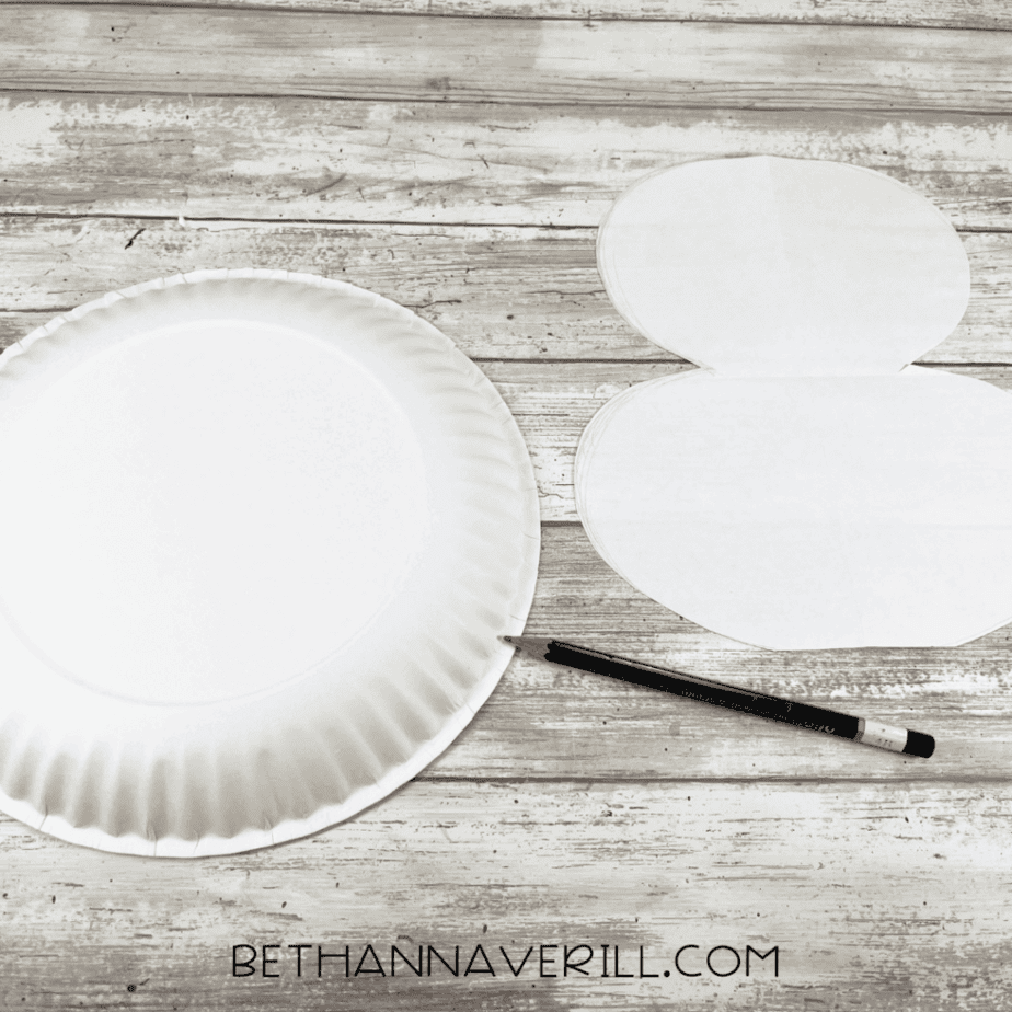 A blank white paper plate on a wooden table with a pencil resting beside it and a puffin body template printed on white paper.