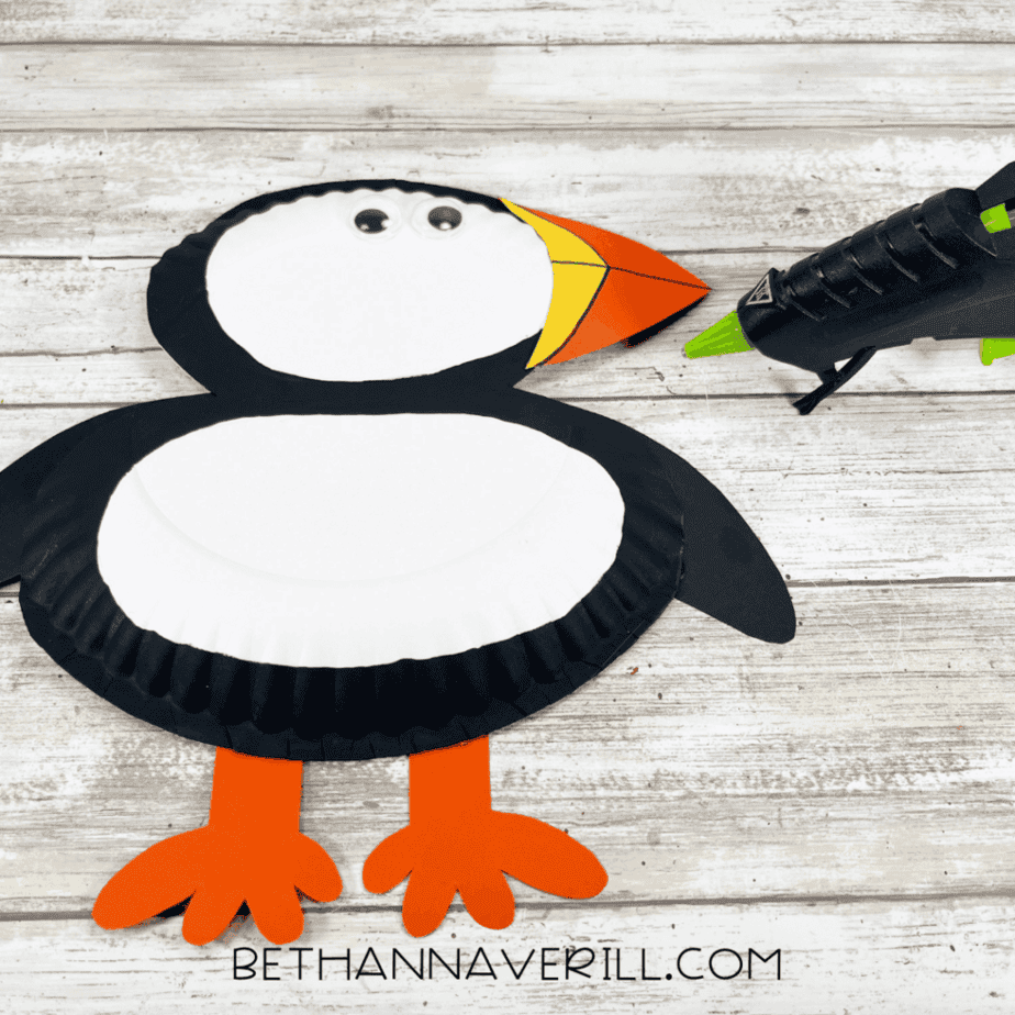 A close view of the puffin with its beak glued on and googly eyes added to the head. A glue gun and a marker are nearby.