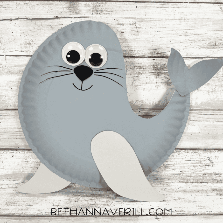 Completed seal paper plate craft with googly eyes, whiskers, tail, and flippers on a wooden background.