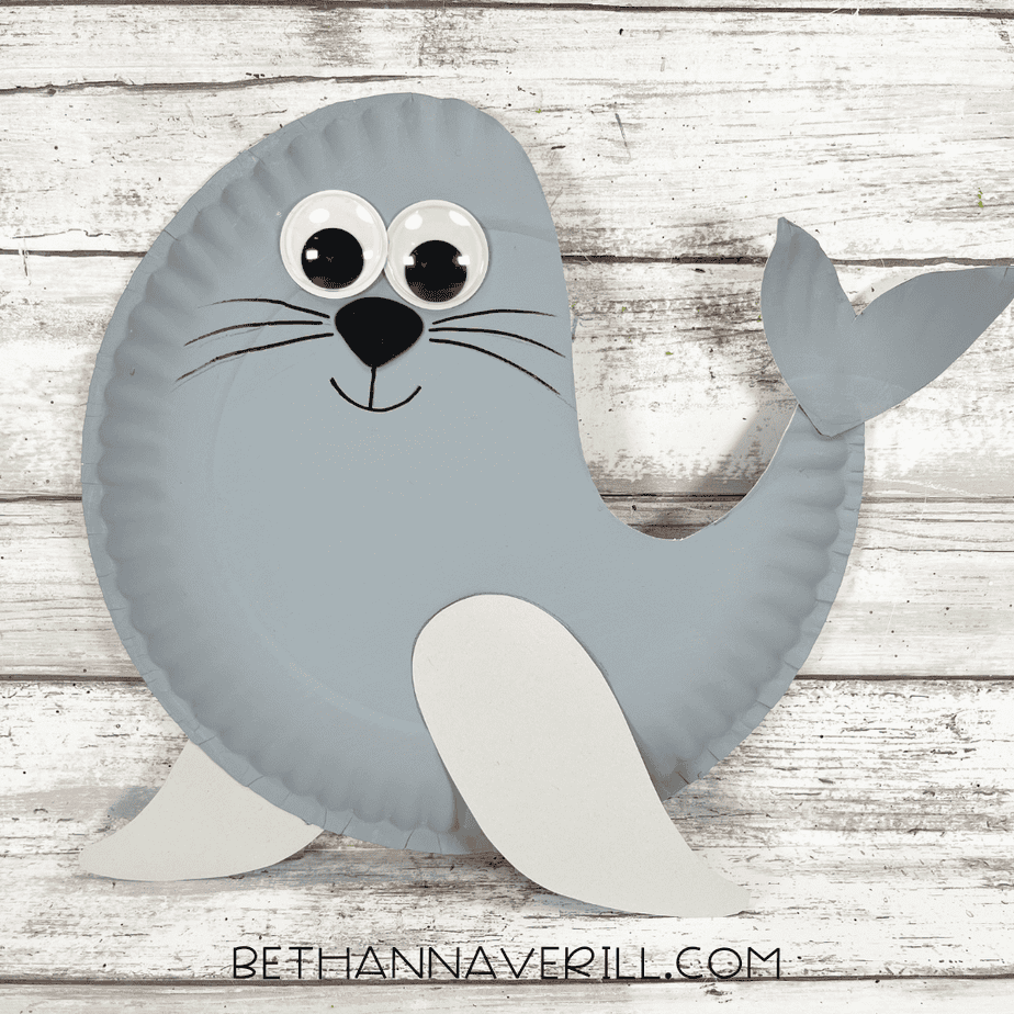 Completed seal paper plate craft with googly eyes, whiskers, tail, and flippers on a wooden background.